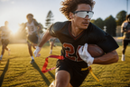 Flag football player carrying the ball upfield in low golden light with defenders behind him